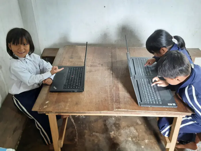 Young students working on laptops at a wooden table, Educere Learning Center