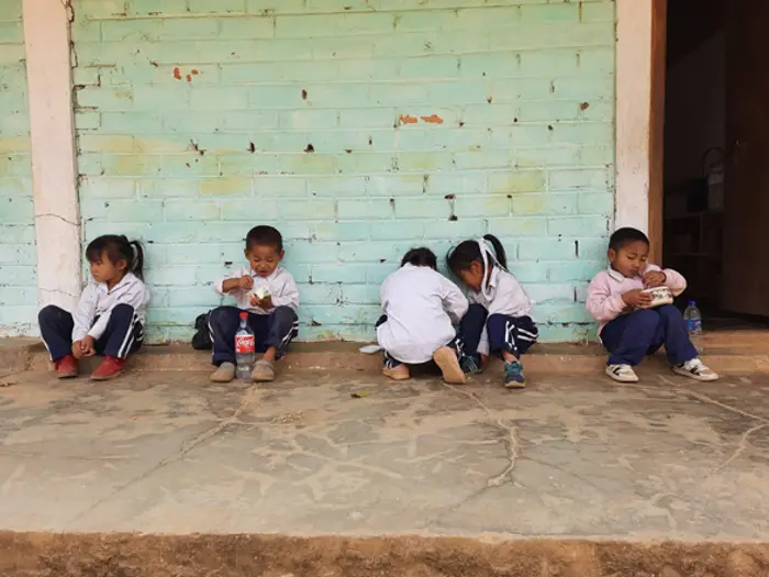 Children sitting along the veranda wall with their books, Educere Learning Center