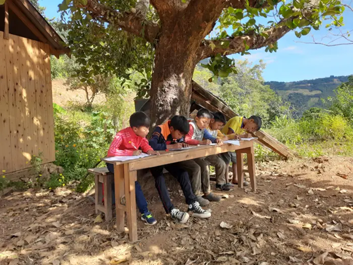 Children studying at tables in the shade of a large tree, Educere Learning Center