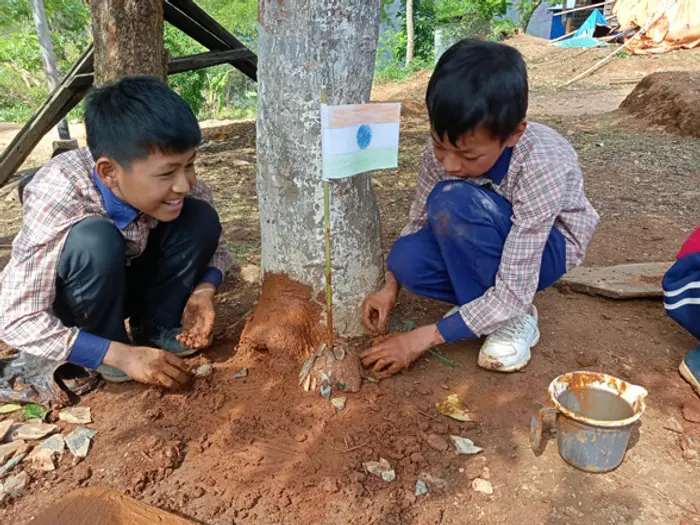 Two boys planting a sapling at the foot of a tree, Educere Learning Center
