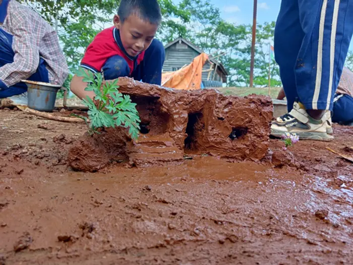 A child shaping clay beds around young plants, Educere Learning Center