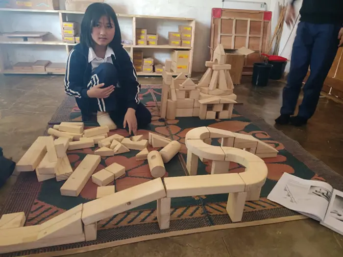 A student with a long wooden-block construction on the classroom floor, Educere Learning Center