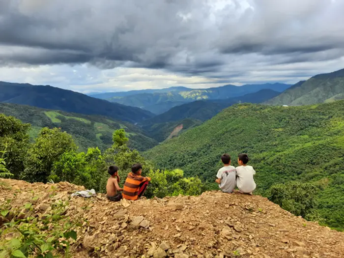 Two children sitting on a ridge looking out over green hills near the village, Educere Learning Center