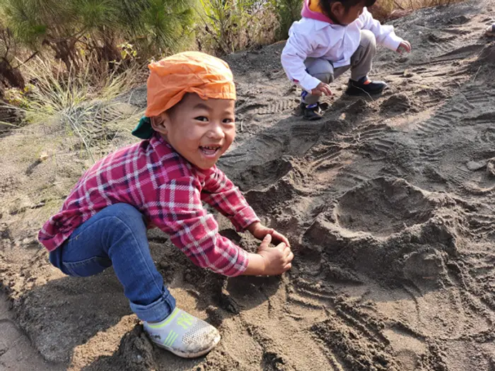 A smiling child playing in the sand outdoors, Educere Learning Center